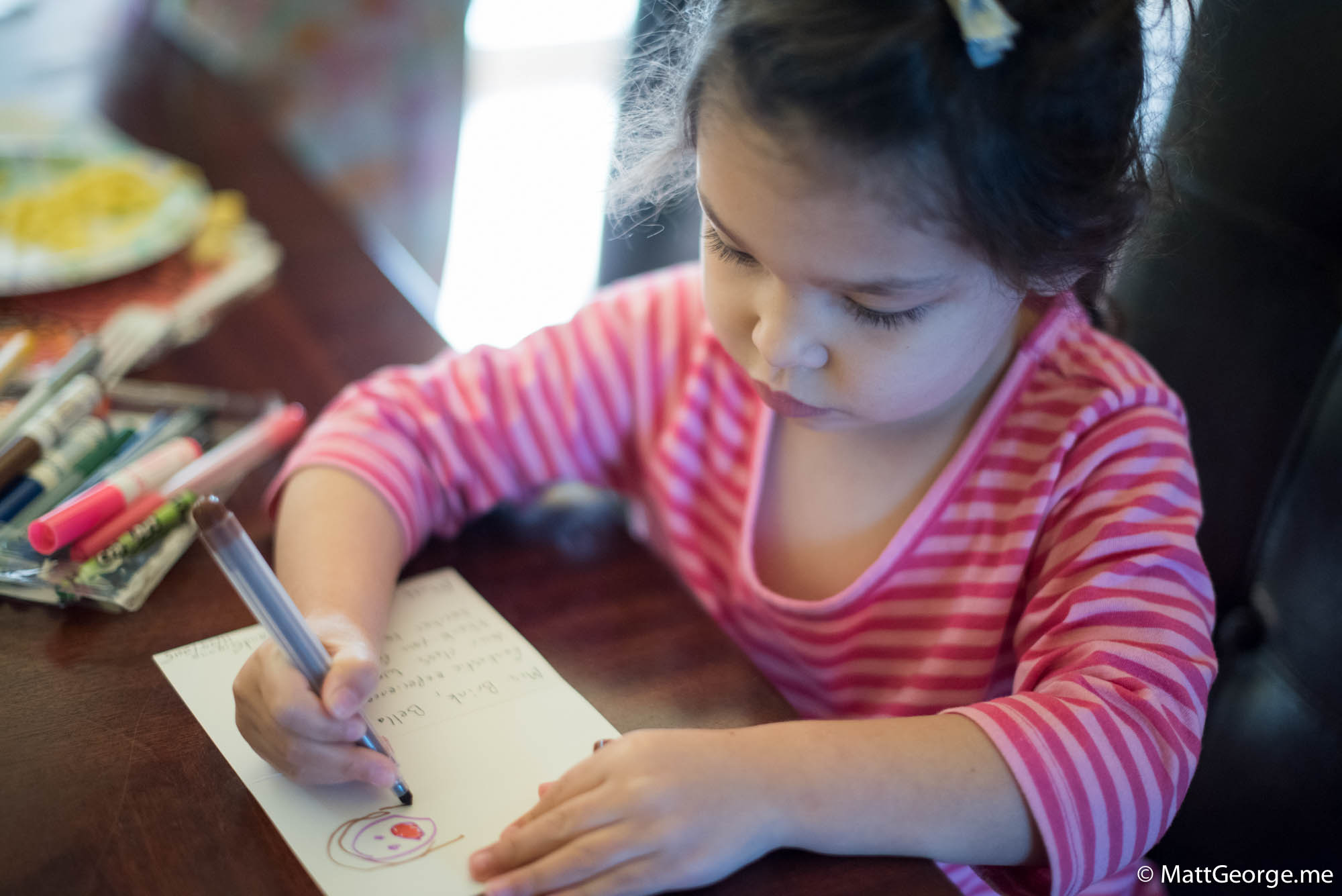 Bella is drawing some hair on a face on a card for her teacher.