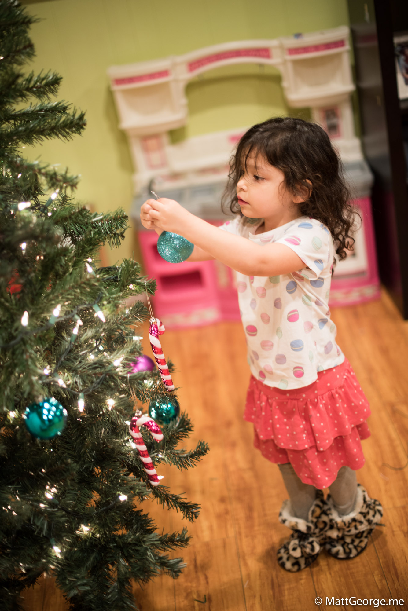 Bella Putting on an Aqua Colored Christmas Bulb Ornament Onto Tree
